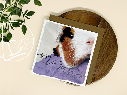 Illustrated card of a black, white and ginger guinea pig. The text says "mwah"